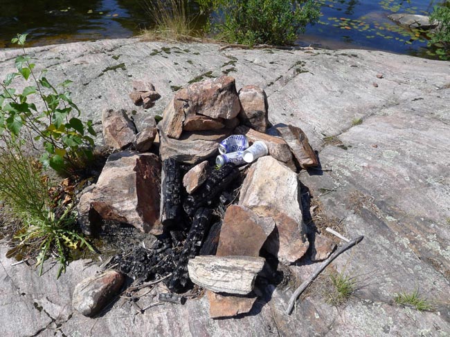 Messy fire circle containing beer cans and garbage, litter