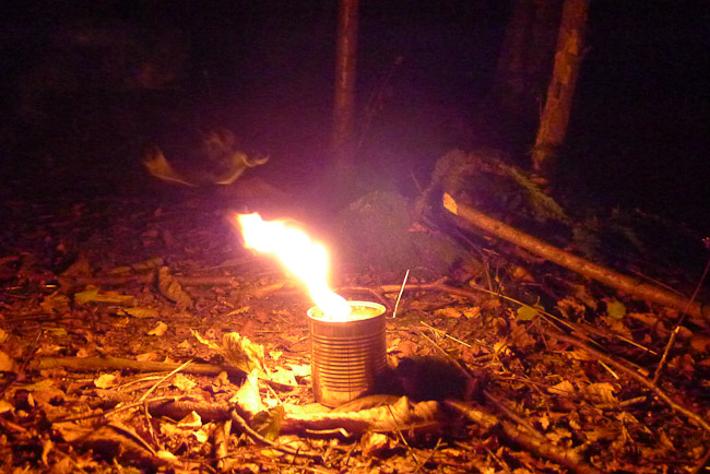 Tin can candle burning at night and illuminating area of woodland