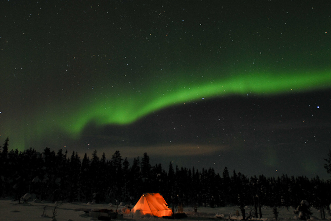 Northern lights over an illuminated tent.