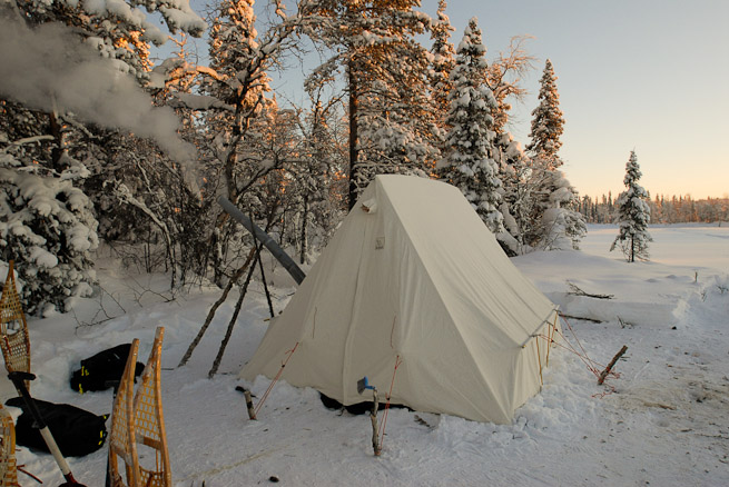 Canvas wall tent in snow with snowshoes and snow shovel