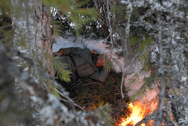 Man lying in front of fire in an improvised shelter