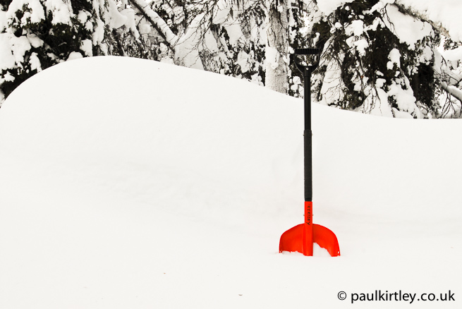 Red coloured Black Diamond snow shovel in white snow