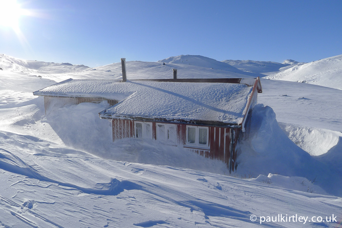 A hut in the snow with lots of spindrift