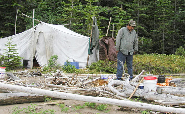 Innu man tends a fire outside a canvas tent
