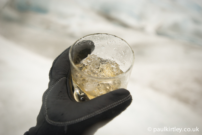 Glass with whisky and glacial ice with out of focus glacier in the background