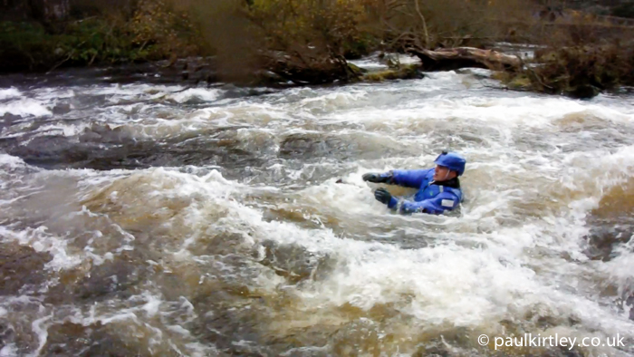 Man in drysuit and helmet being swept down white water rapids