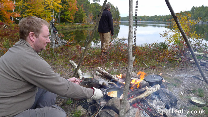 Man cooking pancakes on a campfire with some fall colours in the background