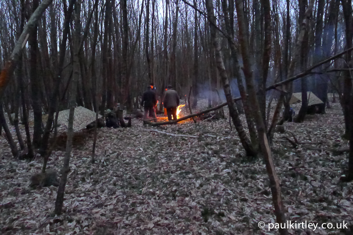 Men in woods standing around camp fire in winter