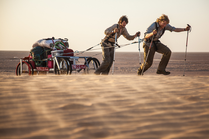 Two men pulling a cart across sand