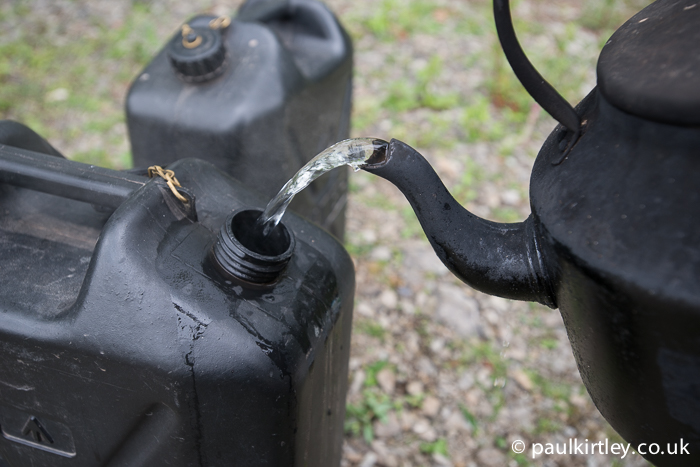 Pouring water from a campfire kettle into a jerry can