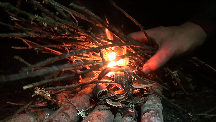 Hand holding sticks over burning birch bark