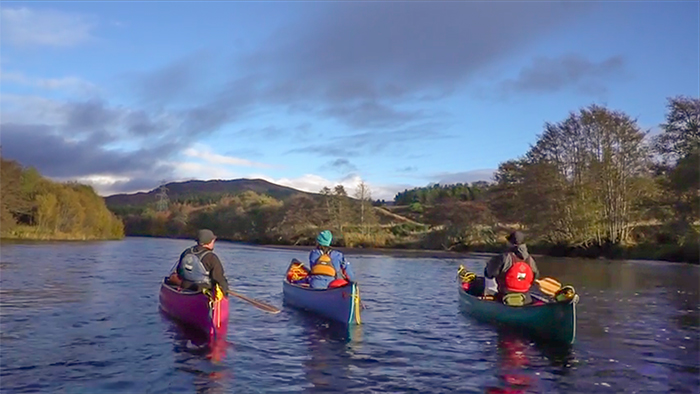 Three canoeists with a blue shy background, illuminated by low autumn sunshine