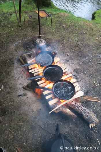 Split wood being used as a griddle in camp underneath frying pans - great campcraft