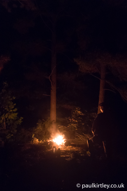 Camp illuminated by campfire with trees