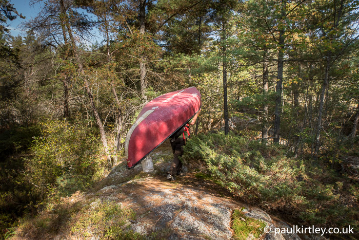 Red canoe being carried through the woods
