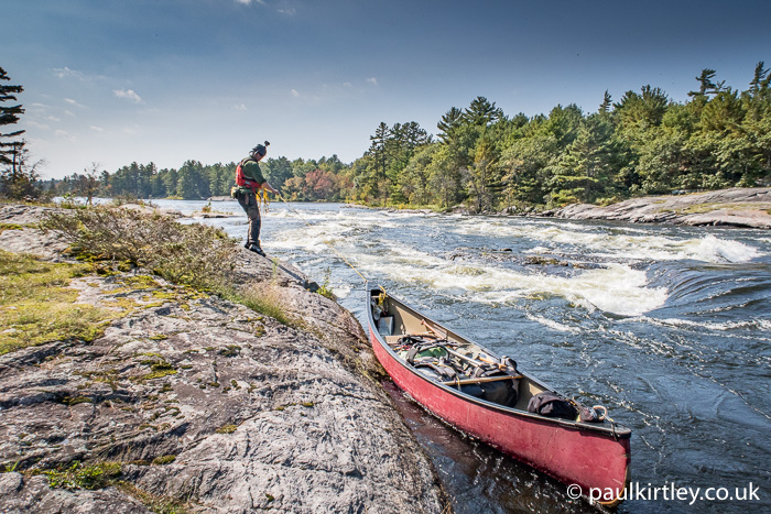 Man lining a canoe down edge of rough rapids