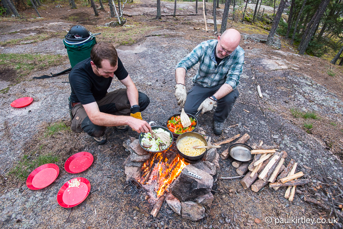 Two men looking happy while cooking on a campfire, surrounded by flat bedrock 