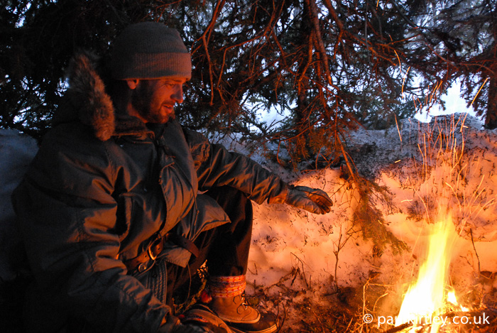 Man inside a tree shelter with a fire