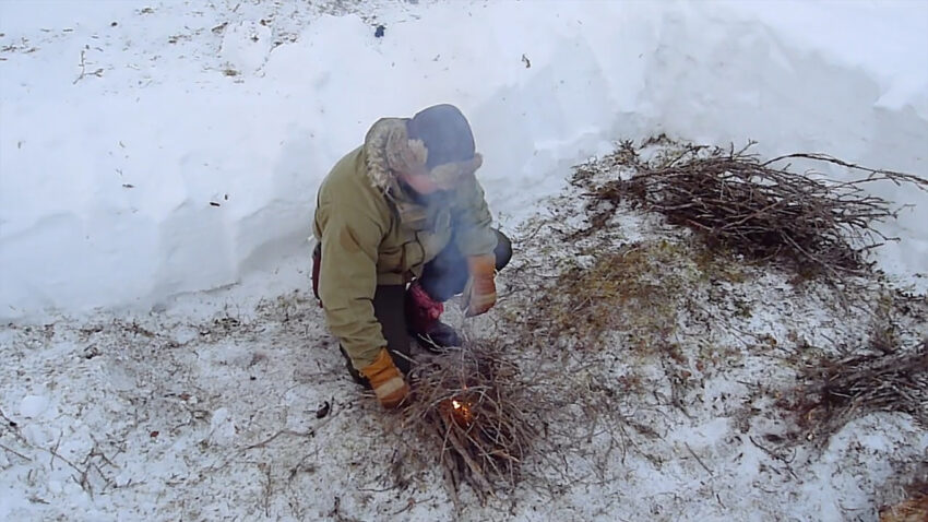 Man lighting fire in clearing dug out of the snow