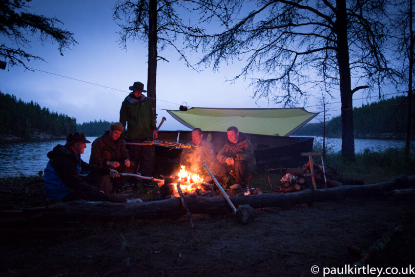 Five men sitting near fire in wilderness, waiting for the weather to change