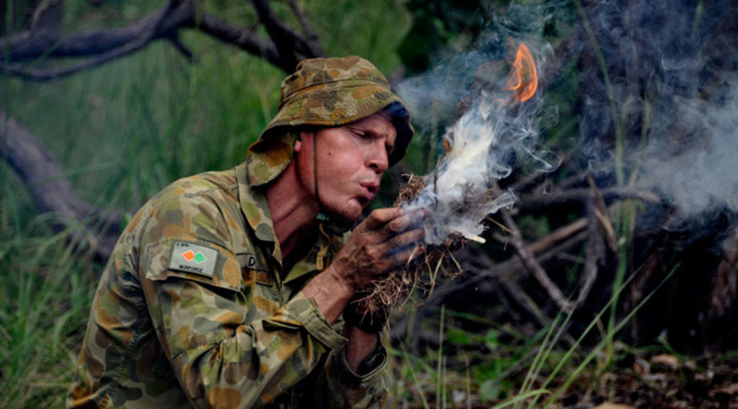 Man in Australian army uniform blowing tinder bundle into flame