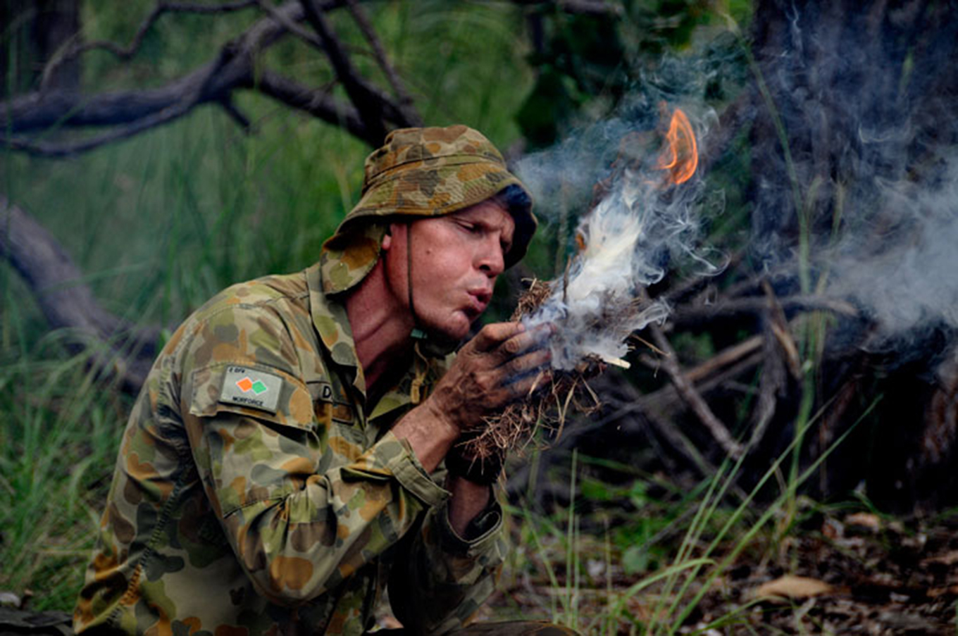 Man in Australian army uniform blowing tinder bundle into flame