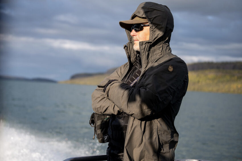 Man staring into distance while riding along on the back of a boat in the wilderness