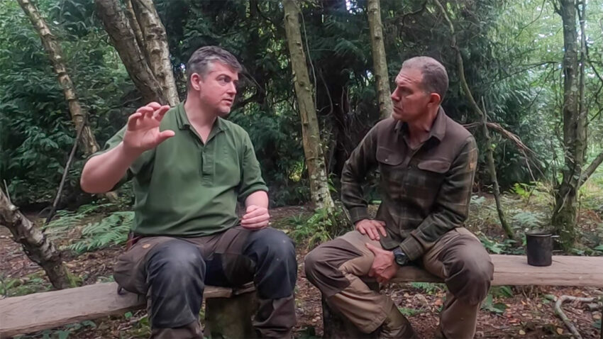Two men sat on benches in the woods talking about bushcraft