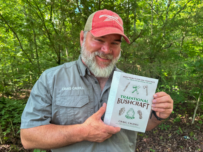 Happy man with beard holding a book called Traditional Bushcraft