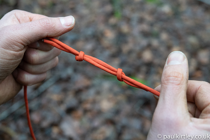 two hands and the makings of a single fisherman's knot in paracord